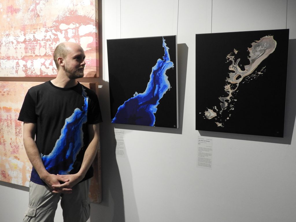 Dan Monceaux stands beside his artworks Hard Lines & Gentle Curves and Lake Gilles, Eyre Peninsula (2017) as exhibited at the Port Pirie Regional Art Gallery